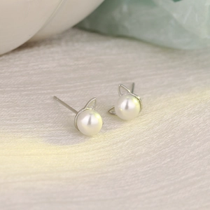 Minimalist silver cat ear pearl stud earrings for women on a soft beige fabric background