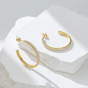 Detailed close-up of golden C-shaped stud earrings with sparkling pave-set white zircons
