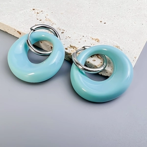 Close-up of light blue resin oval drop earrings on white stone with silver hoops