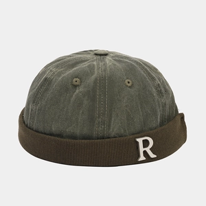 Dettaglio del cappello docker verde oliva con logo della lettera 'R' in metallo argento