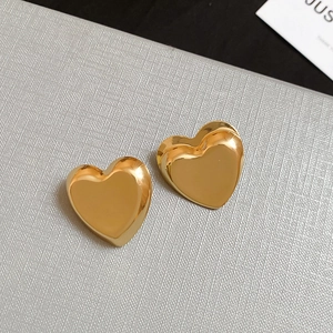Macro view of polished golden heart-shaped stud earrings on grey background