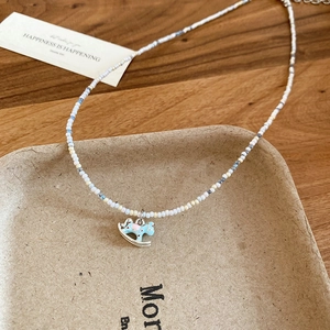 Detail of beaded necklace with a blue rocking horse pendant on a beige jewelry tray