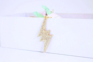 Macro detail of a golden lightning bolt pendant encrusted with sparkling clear rhinestones