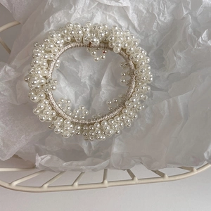 Detailed view of woven beige elastic hair tie with small artificial pearls on paper