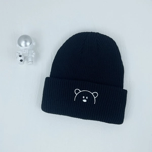 Close-up of black ribbed knit beanie featuring detailed white bear embroidery and thick texture
