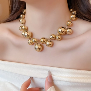 Detail of chunky gold beaded necklace with oversized polished metallic spheres on collar