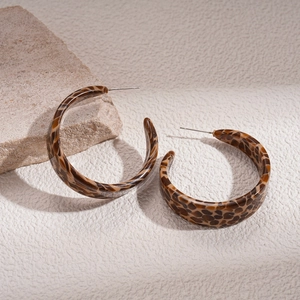 Detail of tortoise shell acetate C-hoop earrings with silver needle on stone surface