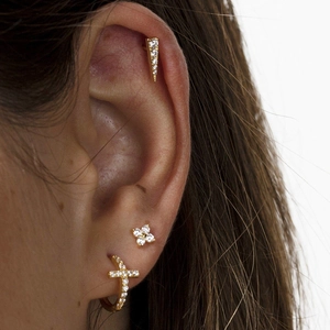 Close-up of gold cross hoop and rhinestone stud earrings set on a model's ear