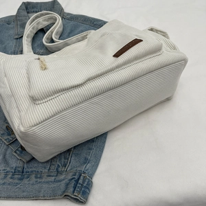 Off-white corduroy tote bag with leather patch on denim jacket background