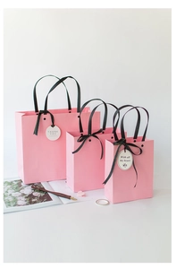 Three sizes of pink gift bags with black silk handles and Thank You tags on a white desk