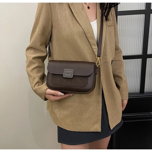 Detail of a brown leather and suede crossbody bag with gold buckle on a model wearing a blazer