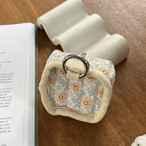Floral fabric storage pouch for cables and earphones with silver metal ring on wood table