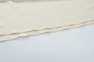 Detail shot of beige fabric hem showing professional overlock stitching and soft texture