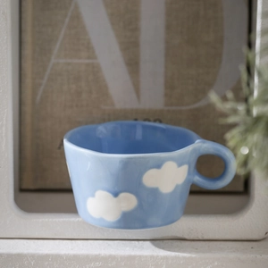 Close-up of blue ceramic mug with white clouds, wavy rim and rounded handle detail