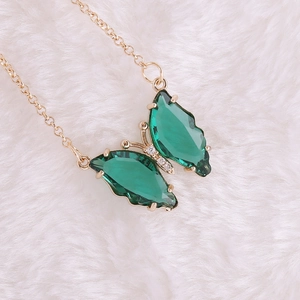 Close-up of green crystal butterfly pendant on a gold chain with diamond accents