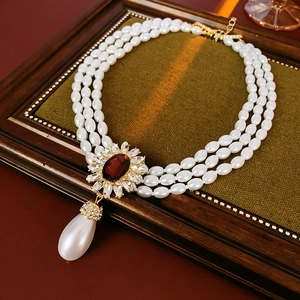 Detail of multi-layer pearl necklace with vintage gold pendant and red gemstone