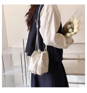Close-up of white hand-woven bucket bag with drawstring closure and soft PU leather texture