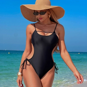 Detail view of sexy black monokini with side cut-outs and lace-up ties on beach