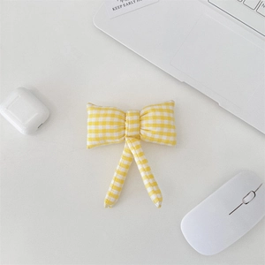 Top view of a yellow checkered bow hair accessory on a clean white desk with modern gadgets