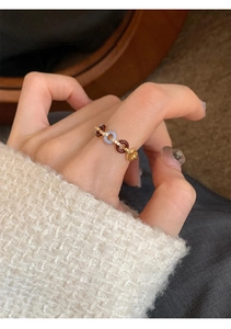 Detail of zircon gold ring with red blue enamel and knot design on hand