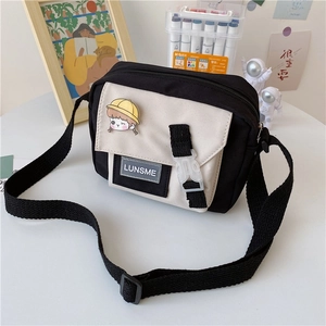 Detail of canvas crossbody bag with contrast colors, plastic buckle and cartoon pin