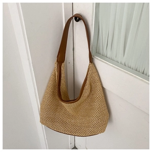 Detailed close-up of khaki woven straw tote bag with brown leather trim on white door