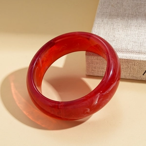 Macro shot of red translucent resin bangle with elegant white ink swirl texture and side lighting