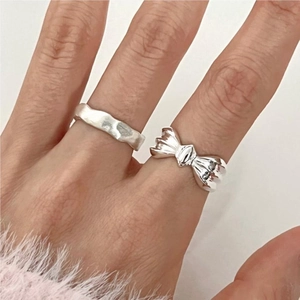 Close-up of 925 sterling silver bow and wavy rings set worn on finger with soft aesthetic