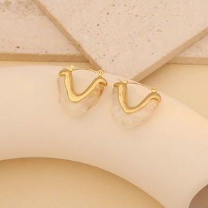 Detail of V-shaped gold earrings with marbled resin texture on a stone pedestal