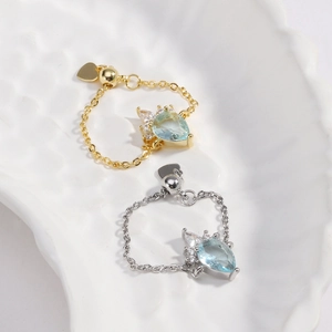 Detail of drop-shaped blue crystal chain rings in gold and silver finish with heart charm