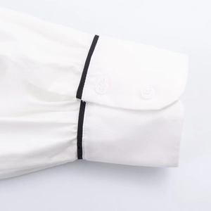 Detail of white cotton shirt cuff with black contrast piping and two clear buttons