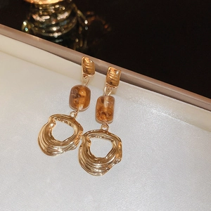 Macro detail of retro amber resin and hollowed golden metal earrings on white fabric