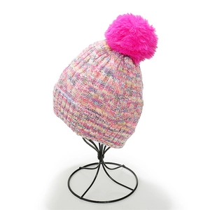 Detail of colorful knitted beanie with a bright pink faux fur pompom on display stand