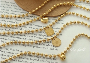 Detail of 18K gold bead chain with heart charm and Elizabeth II coin on a vintage book