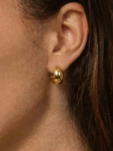 Gros plan de petites boucles d'oreilles en C dorées à l'or fin portées sur le lobe