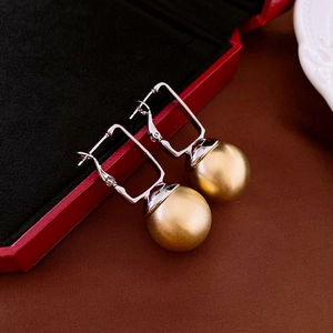 Macro view of geometric drop earrings with gold frosted spheres and silver square hooks