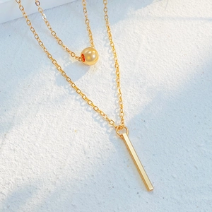 Detailed view of layered gold necklace with geometric square and bead pendants on stone