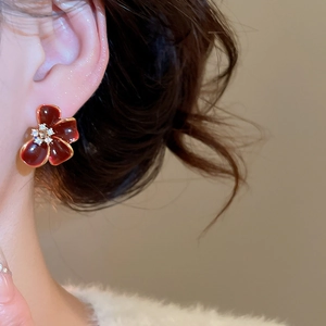Close-up of red enamel flower earrings with gold edges and zircon inlay on model