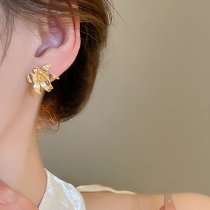 Detail of elegant gold lily flower stud earring with textured petals on model ear