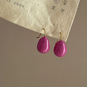 Magenta teardrop enamel earrings with gold metal hooks on a stylish fabric card display