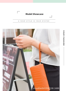 Close-up of an orange crocodile pattern clutch bag held by a model on a city street
