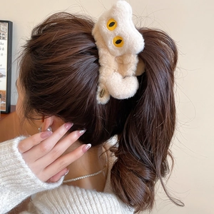 Détail de la pince à cheveux monstre en peluche crème portée sur les cheveux du modèle
