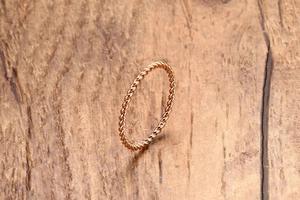 Makroaufnahme eines gedrehten, minimalistischen Seilrings in Roségold auf Holzoberfläche