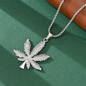 Macro shot of a silver cannabis leaf pendant on a green textured surface necklace