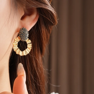 Close-up of golden wrinkled hoop earrings with black pavé crystals on a female model