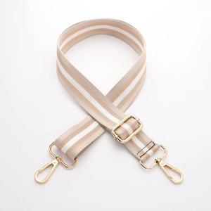 Detail of striped beige and white canvas bag strap with adjustable gold metal hardware