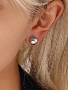 Close-up of a silver spherical ball earring worn on ear with high-polish metallic finish