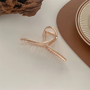 Detailed view of a gold metal hair claw clip with cross-jaw design on a minimalist background