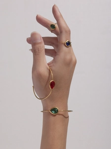 Detail showing gold teardrop glass bangles and square gemstone rings worn on a hand