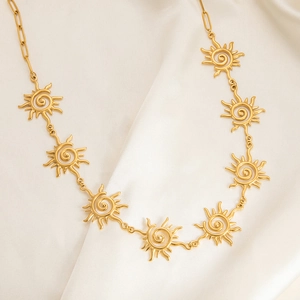 Detail of gold sun pendant necklace with paperclip chain on beige silk background